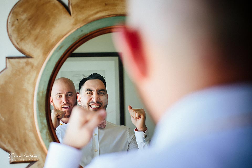 groom happy getting ready and looking at the mirror with best man helping groom